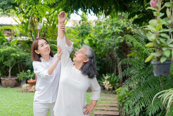 Yaşlı bir Asyalı kadın ve kızıyla arka bahçede egzersiz yapıyor. Mutlu emeklilik kavramı. Bakıcının, birikimin ve sağlık sigortasının özenle. Mutlu bir aile. - Fotoğraf, Görsel