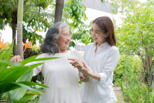 年配のアジア系の女性が娘と一緒に裏庭を歩いている。幸せな退職の概念介護者のケアと貯蓄と高齢者の健康保険で、幸せな家族 - 写真・画像