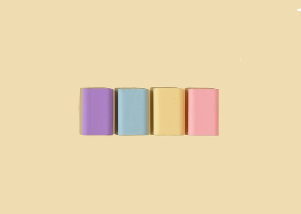 Cztery gumowe gumowe gumki w pastelowych kolorach na jasnożółtym tle. Ogólnokrajowa koncepcja gumowego dnia kasowania. Widok z góry, płaski. - Zdjęcie, obraz