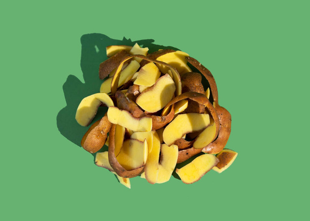 Concept van Stop voedselverspilling dag. Aardappelschillen zijn een van de meest voorkomende afgedankte items tijdens de bereiding van voedsel. Groene achtergrond. - Foto, afbeelding