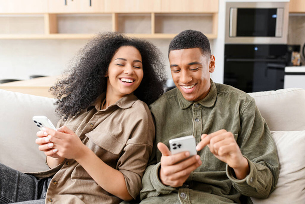 Woman sitting at the couch and looking at the smartphone of her boyfriend. Multiracial couple with gadgets on the couch - 写真・画像