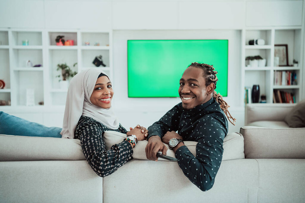 African Couple Sitting On Sofa Watching TV Together Chroma Green Screen Woman Wearing Islamic Hijab Clothes - Photo, Image