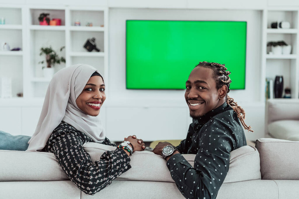 African Couple Sitting On Sofa Watching TV Together Chroma Green Screen Woman Wearing Islamic Hijab Clothes - Foto, immagini