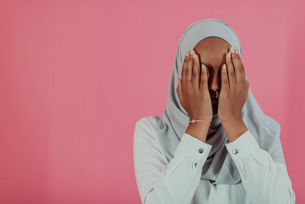 Modern African Muslim woman makes traditional prayer to God, keeps hands in praying gesture, wears traditional white clothes, has serious facial expression, isolated over plastic pink background - Fotó, kép