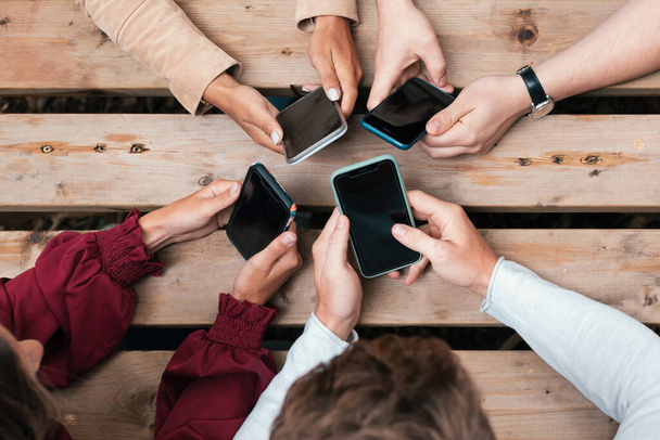 hands of young people in circle on table holding mobile phone - top view of hand using smartphone - Photo, Image