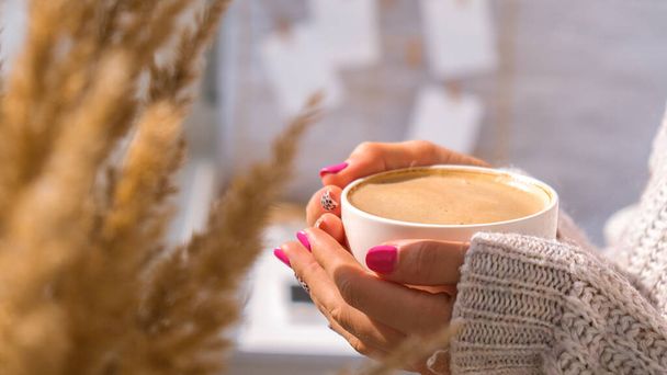 パンパス草とコーヒーと白いカップを保持女性の手。自宅で朝の朝食にカプチーノを飲む。審美的な。居心地の良い家 - 写真・画像