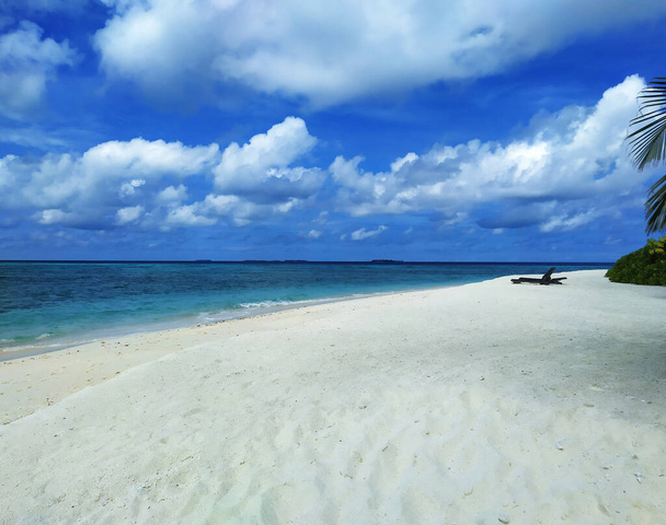 Maldives, the deserted beach with empty sunbeds. A white sand, turquoise ocean and a blue sky. - Photo, Image