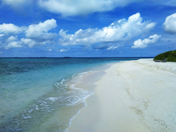 Maldives, the deserted beach with white sand. The turquoise ocean and blue sky with clouds. - Foto, afbeelding