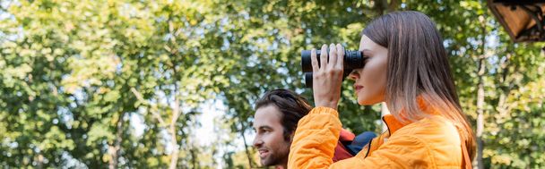 Young traveler looking through binoculars near boyfriend outdoors, banner  - Foto, afbeelding