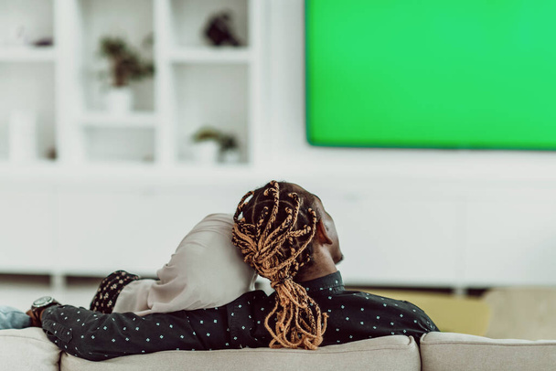 African Couple Sitting On Sofa Watching TV Together Chroma Green Screen Woman Wearing Islamic Hijab Clothes - 写真・画像