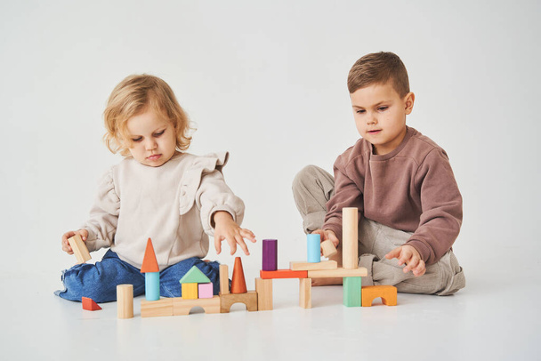 Menina brinca com criança alegre com cubos de madeira de brinquedo no fundo branco. As crianças sorriem e se divertem juntas - Foto, Imagem