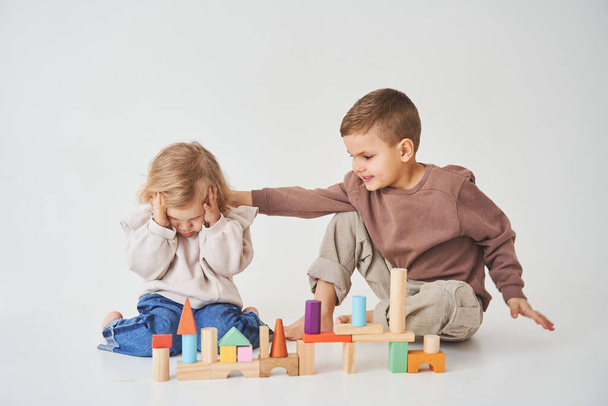 Αγόρι και κορίτσι χαμογελώντας, διασκεδάζοντας και παίζοντας χρωματιστά παιχνίδια τούβλα σε λευκό φόντο. Τα παιδιά χαμογελούν και διασκεδάζουν μαζί. - Φωτογραφία, εικόνα