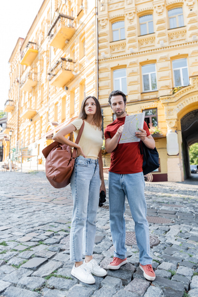 Reisender zeigt mit Rucksack und Fernglas auf Stadtkarte in der Nähe seiner Freundin  - Foto, Bild