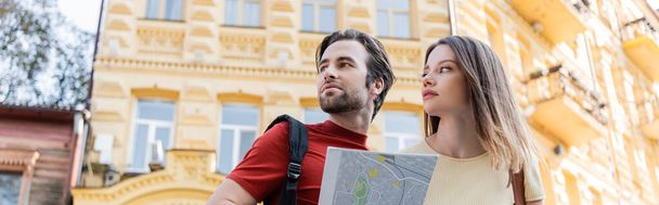 Low angle view of couple of travelers with map looking away on urban street, banner  - Photo, Image