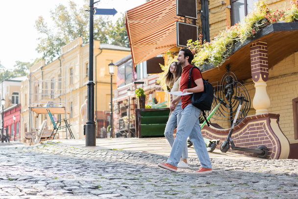 Jóvenes viajeros con mochila y mapa caminando por la calle urbana  - Foto, Imagen