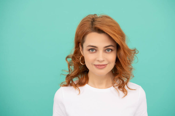 smiling redhead woman with curly hair on blue background - Zdjęcie, obraz