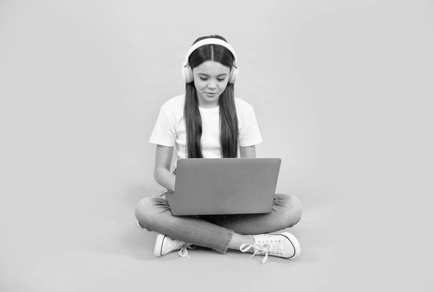 Lächelndes Mädchen benutzt drahtlosen Laptop für Videoanrufe oder hört Webinar über Kopfhörer, zurück zur Schule. - Foto, Bild
