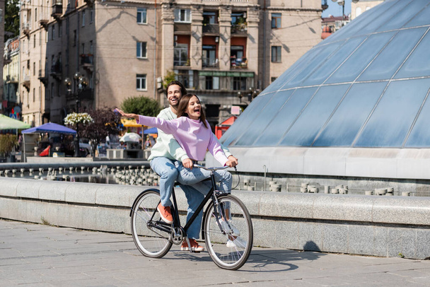 Happy man riding bicycle with excited girlfriend on urban street  - Photo, Image