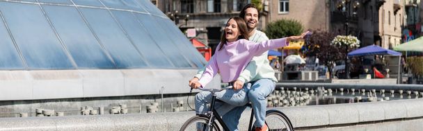 Positive young couple riding bicycle on urban street, banner  - Φωτογραφία, εικόνα