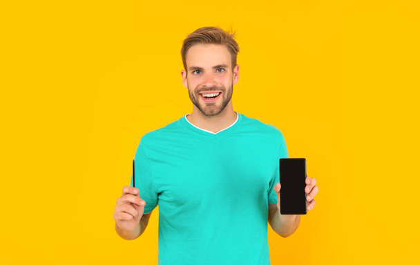 happy guy showing smartphone on yellow background. product proposal. - Φωτογραφία, εικόνα