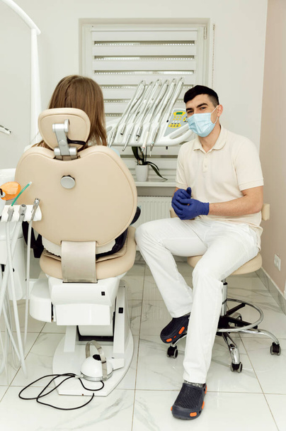 patient at the appointment with a highly qualified dentist. a girl sits in a dental chair talking to a doctor. doctor in a mask and gloves listens to a patient - Foto, Bild