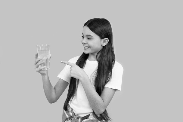 χαρούμενο παιδί που δείχνει με το δάχτυλο ένα ποτήρι νερό για να διατηρεί την καθημερινή ισορροπία του νερού στο σώμα, ενυδάτωση. - Φωτογραφία, εικόνα