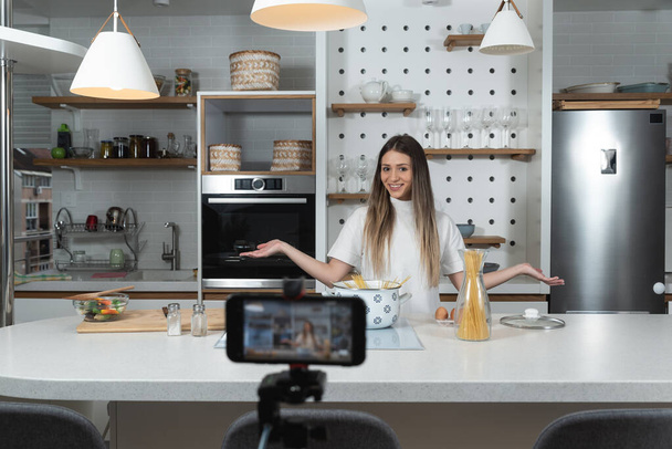 Молода жінка відеоблогерів про приготування їжі у своїй квартирі готує їжу на кухні та робить відео-відеозапис зі смартфоном як творцем онлайн-контенту для Інтернету. Жіночий інфлюенсер приготування їжі
. - Фото, зображення