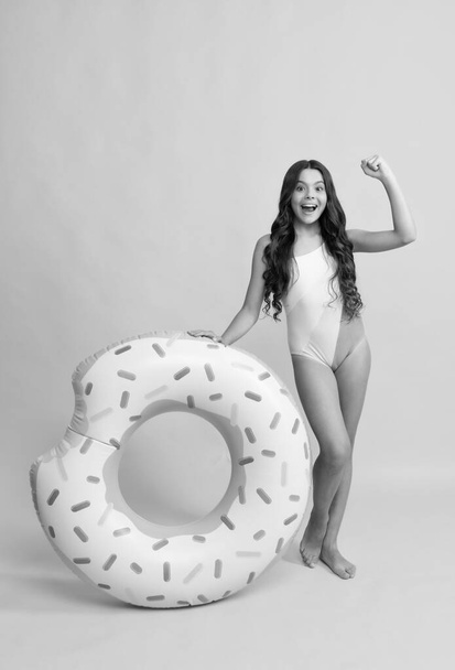 happy beach kid in swimsuit with doughnut inflatable ring on yellow background, summer vacation. - Photo, Image