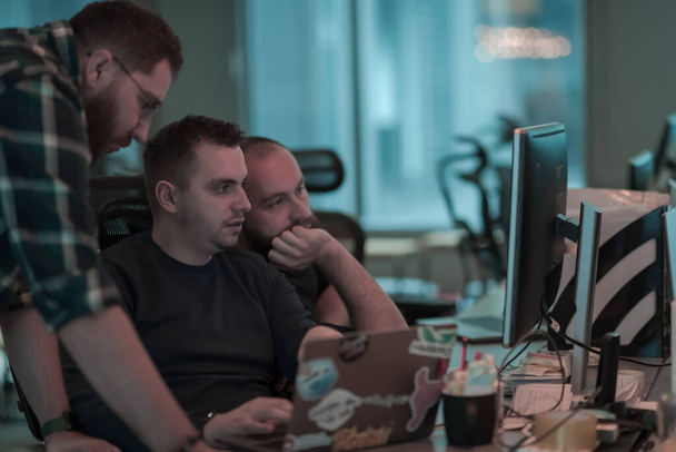 Uma foto de três homens olhando atentamente para um computador enquanto estavam sentados em um escritório moderno. Foco seletivo  - Foto, Imagem