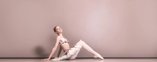 young beautiful graceful caucasian ballerina practice ballet positions in tutu skirt. Classical Ballet dancer sitting on the floor in the studio - Foto, Imagem