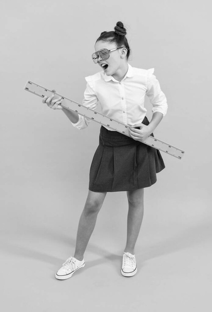 ευτυχής έφηβος κορίτσι φορούν στολή και γυαλιά κρατώντας χάρακα μαθηματικά σε μπλε φόντο, μέτρηση - Φωτογραφία, εικόνα