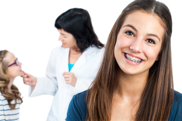 Teen girl with braces and doctor with patient in background. - Фото, изображение