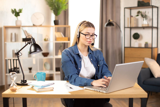 Pretty young woman using headset and laptop for video call, working at home - Foto, Imagen