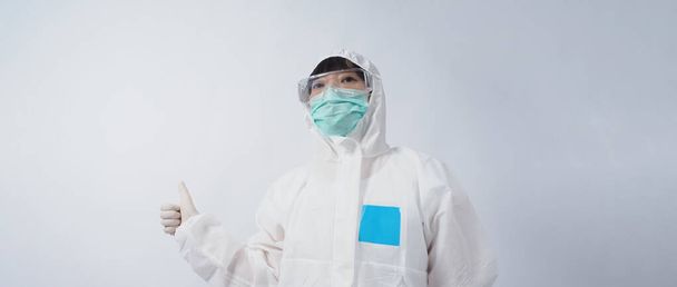 Medico in tuta PPE indossa guanti di gomma medica bianca e occhiali trasparenti e maschera facciale verde N95 per proteggere la pandemia di Coronavirus. gesto fare segno di mano. Rappresentare vittoria vincere sul virus. Isolato. - Foto, immagini