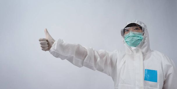 Médico en traje de PPE con guantes de goma médica blanca y gafas transparentes y máscara facial N95 verde para proteger el Coronavirus pandémico. gesto hacer la señal de la mano. Representa la victoria sobre el virus. Aislado. - Foto, Imagen