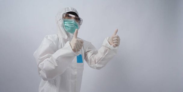 Arzt im PSA-Anzug mit weißen medizinischen Gummihandschuhen und klarer Brille und grüner N95-Gesichtsmaske zum Schutz vor Coronavirus-Pandemie. Geste Handzeichen setzen. Stellvertretender Sieg über das Virus. Isoliert. - Foto, Bild