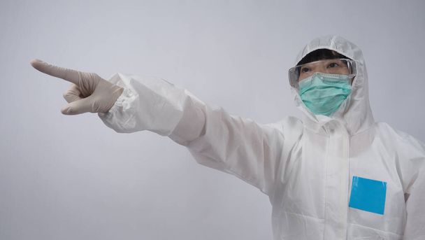 Médico en traje de PPE con guantes de goma médica blanca y gafas transparentes y máscara facial N95 verde para proteger el Coronavirus pandémico. gesto hacer la señal de la mano. Representa la victoria sobre el virus. Aislado. - Foto, Imagen