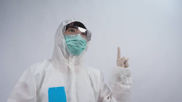 Médico en traje de PPE con guantes de goma médica blanca y gafas transparentes y máscara facial N95 verde para proteger el Coronavirus pandémico. gesto hacer la señal de la mano. Representa la victoria sobre el virus. Aislado. - Foto, imagen