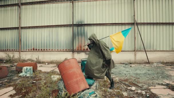 Soldado con máscara de gas ondea bandera ucraniana en un almacén de guerra - Metraje, vídeo