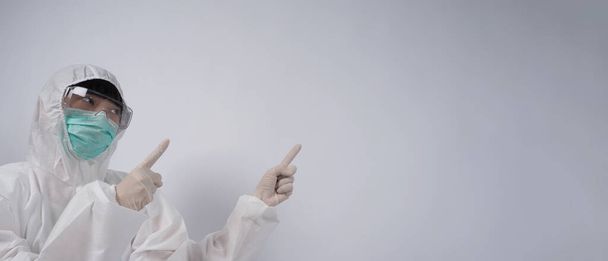 Médecin en costume EPI portant des gants en caoutchouc médical blanc et des lunettes claires et un masque facial vert N95 pour protéger le coronavirus pandémique. geste faire signe de la main. Représenter victoire sur le virus. Isolé. - Photo, image