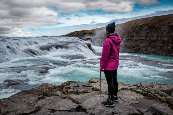 girl in a purple jacket looks at the waterfall Gullfoss in Iceland - Фото, изображение