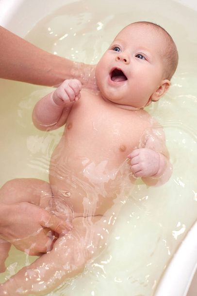 mother bathes her baby in a white small plastic tub - Fotoğraf, Görsel