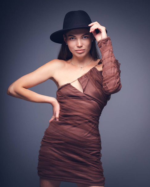 Retrato de estudio de moda de una hermosa joven con sombrero negro sobre un fondo gris - Foto, imagen