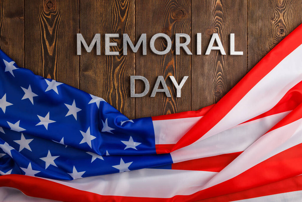 the words memorial day laid with silver metal letters on wooden board surface with crumpled usa flag - Foto, afbeelding