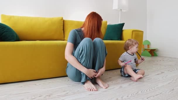 Ginger woman mother sitting on the floor with her baby son holding pens - Footage, Video