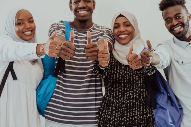 Group portrait of happy African students standing together against a white background and showing ok sign thumbs up girls wearing traditional Sudan Muslim hijab fashion - Photo, Image