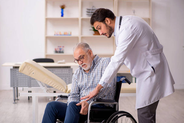 Anciano en silla de ruedas visitando al joven médico masculino - Foto, Imagen