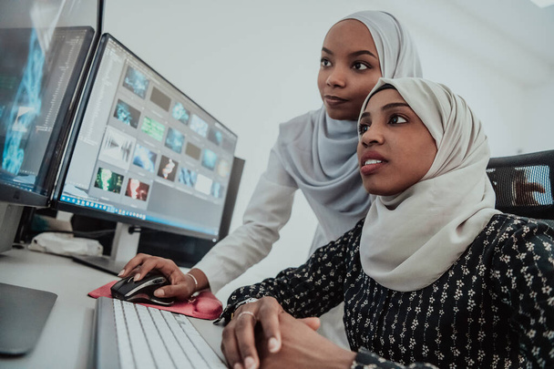 Friends at the office two young Afro American modern Muslim businesswomen wearing scarf in creative bright office workplace with a big screen - Φωτογραφία, εικόνα