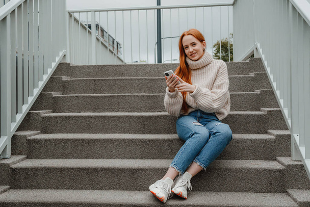Close-up van glimlachend aantrekkelijk meisje met lang haar praten op mobiele telefoon terwijl buiten staan in een straat van de stad. Een mooie glimlachende vrouw die door een drukke straat loopt. Warschau. Polen. - Foto, afbeelding