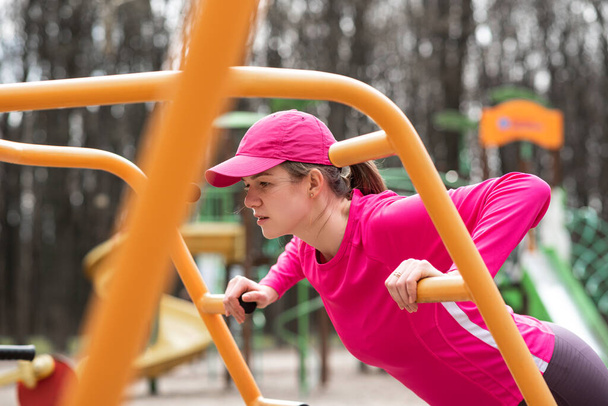 Jeune femme heureuse et forte portant des vêtements roses fait push-ups à l'extérieur à la formation au sol sport ses muscles de la poitrine - Photo, image
